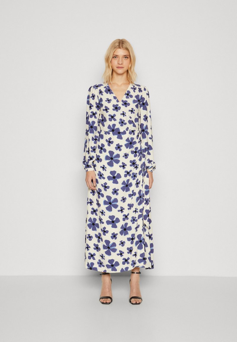 Robe à manches longues, décolleté en V, crème avec un imprimé floral bleu foncé. Tissu léger, corsage ajusté et jupe fluide. Accentuée par un détail à nouer.
