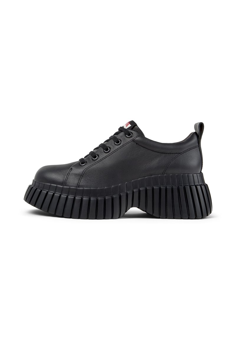 Sneaker in pelle nera con suola spessa e rigata e punta rotonda. Caratteristiche includono design con lacci e un piccolo anello sul retro.