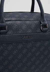 Sac en cuir texturé bleu marine avec un motif de logo subtil, doté de deux poignées courtes et d'une fermeture éclair argentée.