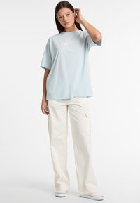Lysblå oversized t-shirt med korte ærmer, der har et diskret logo. Sammen med creméfarvede cargo-bukser med sidelommer.
