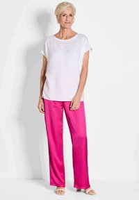 Witte top met korte mouwen en rhinestone accenten, gecombineerd met roze satijnen wijde broek en beige sandalen. Eenvoudig, ontspannen ontwerp, gladde textuur.