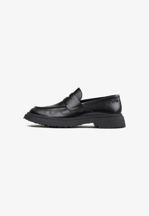 Mocasín de cuero negro con suela de goma gruesa, costuras decorativas en la parte superior y una tira tipo penny en la parte superior.