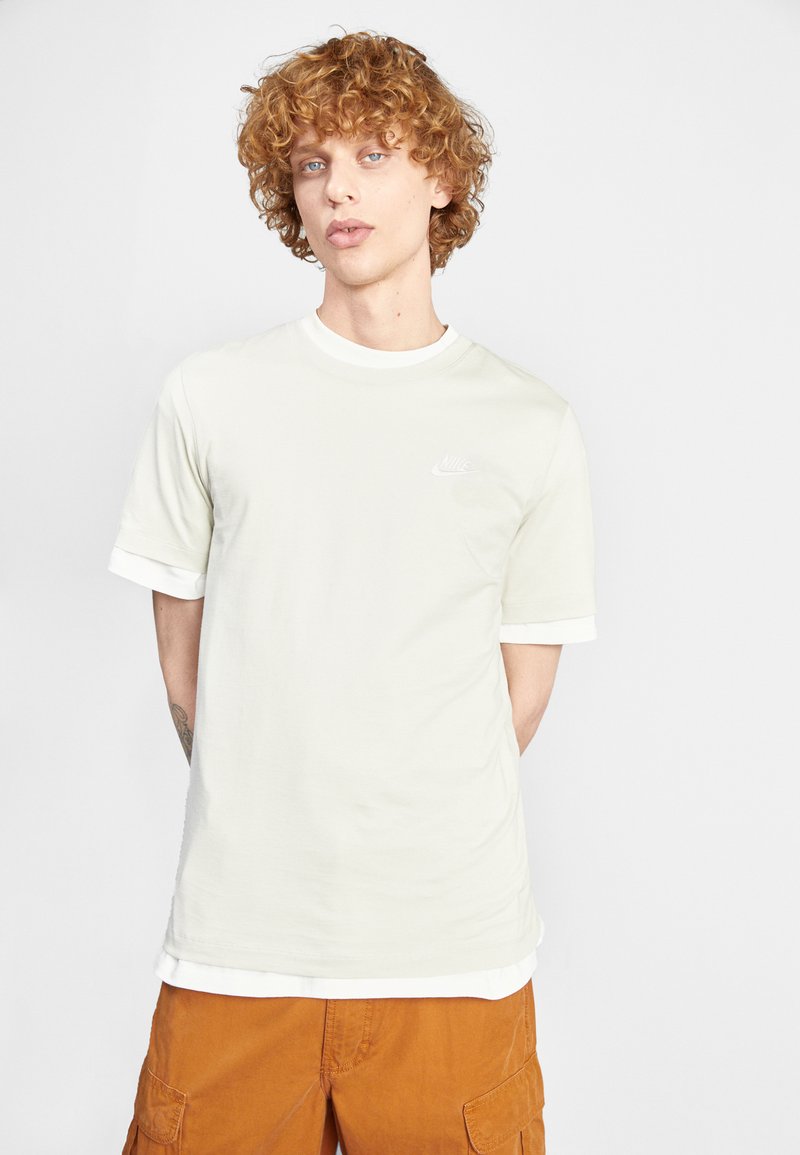 Svetlozelené tričko s bielym okrúhlym golierom a rukávmi. Na hrudi je malá biela logo Nike. Hladká bavlnená zmesová tkanina.