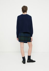 Granatowy sweter o skróconym kroju, zestawiony z zielono-niebieską spódnicą w kratę. Obuwie to czarne buty i ciemne skarpetki o fakturze.