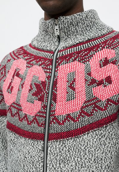 Grijze gebreide trui met hoge kraag, voorzien van een gedurfde roze en rode grafische patroon. Een zichtbare ritssluiting loopt over de voorkant.