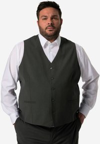 Graue Weste mit V-Ausschnitt, sechs Knöpfen und zwei Taschen. Getragen über einem weißen Hemd. Glatte Textur, taillierte Passform.