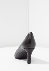 Chaussure à talon haut en cuir noir avec un bout pointu et un talon aiguille de 3 pouces. Texture lisse et détails de conception minimaux. Logo de la marque visible.