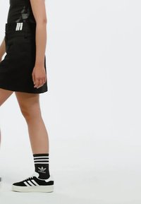 Černá riflová sukně s přiléhavým střihem, kombinovaná s bílými a černými teniskami Adidas a pruhovanými černými ponožkami s logem Adidas.