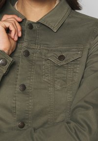 Oliven grøn jakke lavet af slidstærkt stof med krave, frontlukning med knapper og brystlomme med klap og knapdetalje.