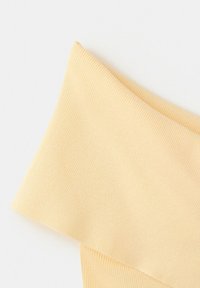Tissu en maille côtelée jaune clair plié en diagonale sur un fond blanc.