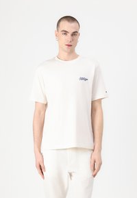 Šviesiai smėlinis medvilninis marškinėliai trumpomis rankovėmis su mėlyna "Hilfiger" logotipu siuvinėtu kairėje krūtinėje, laisvas kirpimas.