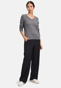 Szary sweter dzianinowy z dekoltem w kształcie V, zestawiony z czarnymi spodniami o szerokich nogawkach. Model stoi z rękami w kieszeniach, nosząc białe trampki.