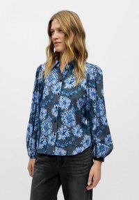 Camicia a bottoni floreale in tonalità di blu su uno sfondo scuro. Presenta maniche a sbuffo e una vestibilità comoda, realizzata in tessuto leggero.