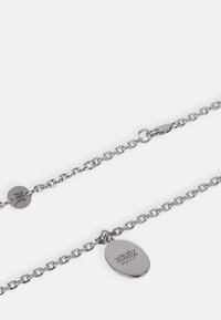 Sølvkjede med oval anheng. Har en teksturert overflate, en lås med clasp og gravert merking på anhenget.