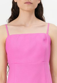 Rosa ärmlös klänning med fyrkantig halsringning, tillverkad av lätt tyg med en mjuk textur och enkla, rena linjer.