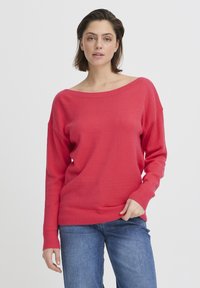 Pull rouge à col bateau avec poignets et ourlet côtelés, en tissu tricoté doux. Associé à un jean bleu. Design simple, sans motifs.