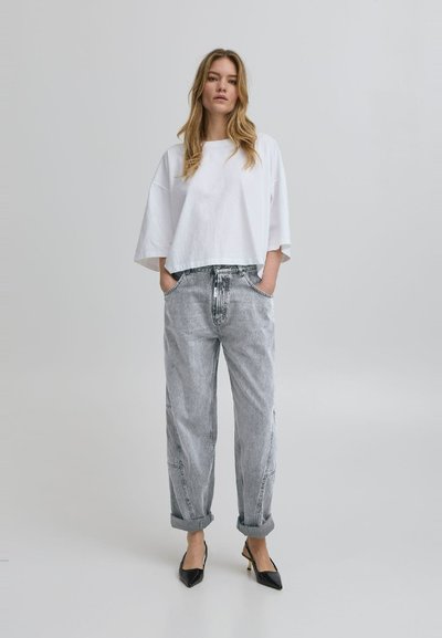 White cropped t-shirt with wide sleeves, paired with light gray high-waisted jeans. Black pointed-toe heels complete the outfit.