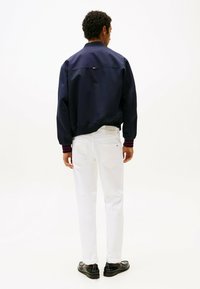 Giacca bomber navy con polsini a coste, abbinata a jeans bianchi e scarpe nere. La giacca presenta un delicato dettaglio con logo sul retro.