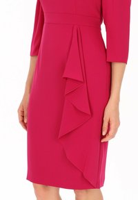 Fuksjowa sukienka z rękawami o długości trzy czwarte; posiada drapowany detal z falbaną po boku, wykonana z gładkiego, teksturowanego materiału.