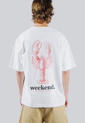 Osoba nosząca białą koszulkę z dużym czerwonym nadrukiem homara i słowem „weekend” nadrukowanym poniżej na plecach.