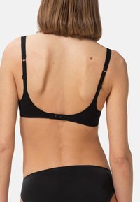 Svart behå med justerbara axelband, låg ryggdesign och hake-och-ögla-stängning. Materialet verkar mjukt med en slät textur.