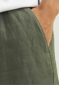 Olivgröna linnebyxor med en strukturerad yta och sidoficka, som visar en avslappnad passform och rena sömdetaljer för hållbarhet.