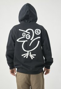 Schwarzer Kapuzenpulli mit einem großen, weißen abstrakten Vogel-Design auf dem Rücken, aus weichem Material mit lockerer Passform und verstellbarem Kapuzenzug.