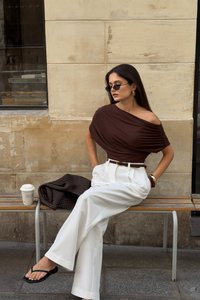 Rjava bluza brez naramnic, bele široke hlače, črne japonke. Dodatki vključujejo okrogle uhane in temno torbo. Kava skodelica v bližini.