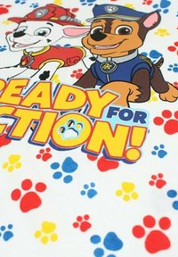 Tissu sur le thème de dessins animés avec un fond blanc, comportant des empreintes de pattes en rouge, bleu et jaune, ainsi que des illustrations de deux chiens. Le texte indique "PRÊTS POUR L'ACTION !"