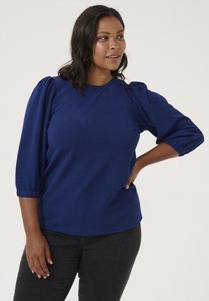 Top blu navy con maniche a palloncino ¾, scollatura rotonda, tessuto testurizzato e vestibilità comoda, abbinato a pantaloni neri.