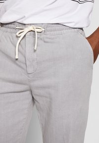 Pantaloni corti in tessuto grigio con vita elastica e cordino bianco. Presentano tasche laterali e una finitura liscia e testurizzata.