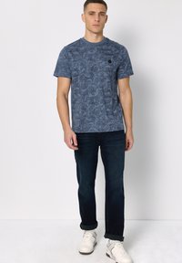 Tmavě modré tričko s texturovaným vzorem, s krátkými rukávy a kulatým výstřihem, doplněné tmavými džíny a bílými teniskami.