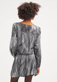 Černobíle vzorované šaty s dlouhými rukávy, volný střih a nabíraným pasem. Texturovaná látka s jemným leskem.