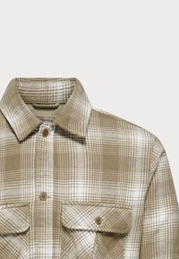Camisa de franela a cuadros marrón y blanca con cuello, dos bolsillos en el pecho y cierres de botón. La textura de la tela parece suave y de peso medio.