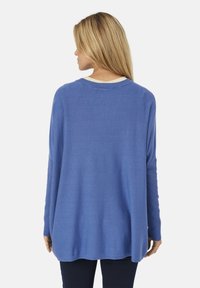Suéter azul de manga larga con un ajuste relajado y acentos de canalé en las muñecas. La tela suave cae hasta un dobladillo ligeramente curvado.