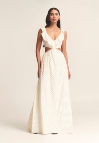 Vestido maxi blanco con lunares negros, escote fruncido, sección media abierta y falda fluida. Hecho de tela ligera, diseñado para la elegancia.