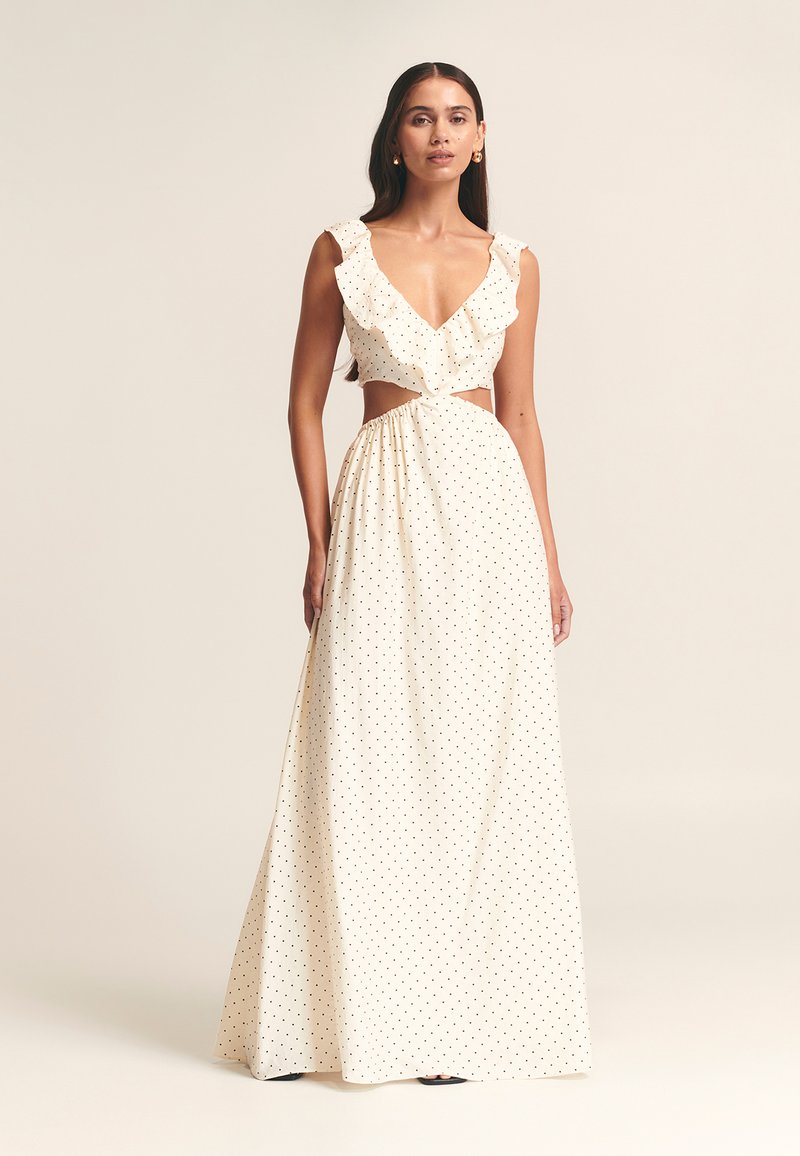Vestido maxi blanco con lunares negros, escote fruncido, sección media abierta y falda fluida. Hecho de tela ligera, diseñado para la elegancia.