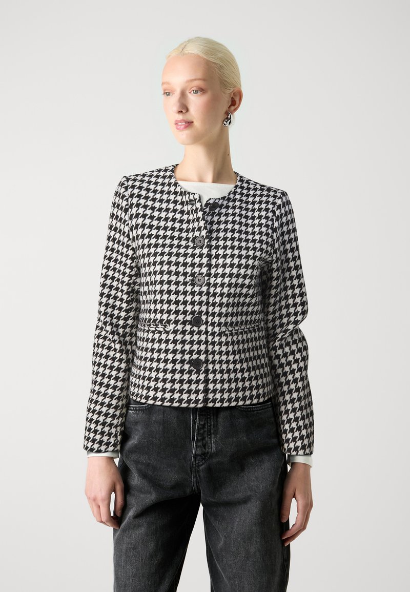 Swarte og kvite houndstooth-jakke med rund hals, frontknappar og lange ermer. Kombinert med grå høgfrelste bukser.