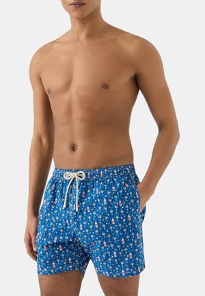 Uomo senza maglietta che indossa pantaloncini da bagno blu con coulisse bianca e motivo di piccole bottiglie e fiori.