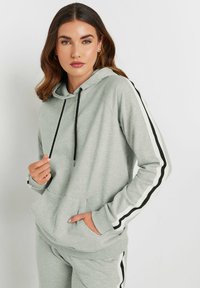 Sudadera gris claro con cordones negros, rayas laterales y un bolsillo frontal. Material suave, corte casual, con puños y dobladillo acanalados.