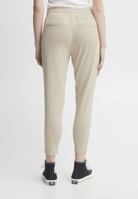 Beige joggers med resårmidja och två bakfickor, tillsammans med svarta högklackade sneakers. Slät struktur och slim fit-design.