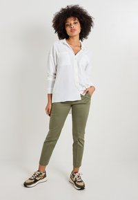Chemise blanche à manches longues avec deux poches poitrine, associée à un pantalon tapered vert olive et des baskets multicolores avec une tige texturée.