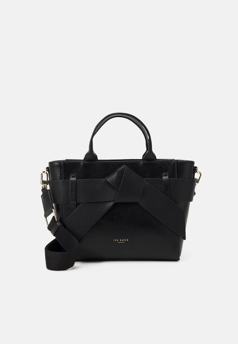Sac à main en cuir noir avec une forme structurée, doté d'une sangle texturée bien visible sur le devant et d'un détail logo en or à la base.