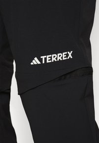 Juodos lauko kelnės su sulaikytos linijos dizainu, turinčios užtrauktuku užsegamą kišenę ir baltą "TERREX" logotipą ant šlaunies. Minkšta, patvari medžiaga.