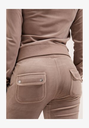 Pantaloni beige vellutati con un design aderente, accentuati da due tasche posteriori, ciascuna con chiusure a pressione in argento e cuciture testurizzate.