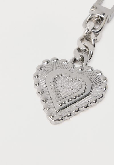 Ασημένιο μεταλλικό μπρελόκ με καρδιά ως μενταγιόν, διακοσμημένη με ανυψωμένες κουκκίδες και χαραγμένες γραμμές.