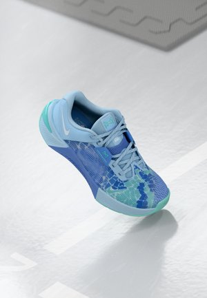 Sapato atlético azul claro com uma parte superior texturizada, design em malha e detalhes verdes. Apresenta atacadores e uma sola de borracha sólida.