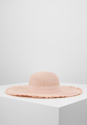 Chapeau de paille tissé à larges bords, rose pâle, avec un ruban lisse, présenté sur un socle blanc contre un fond uni.