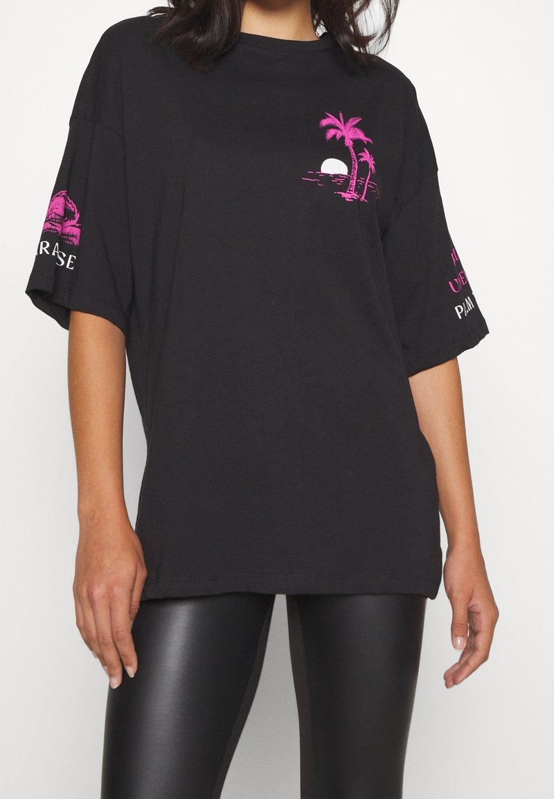 T-shirt noir oversize avec graphique rose de palmier et de soleil sur la poitrine, texte et motif roses sur les manches, porté avec un pantalon en cuir noir.