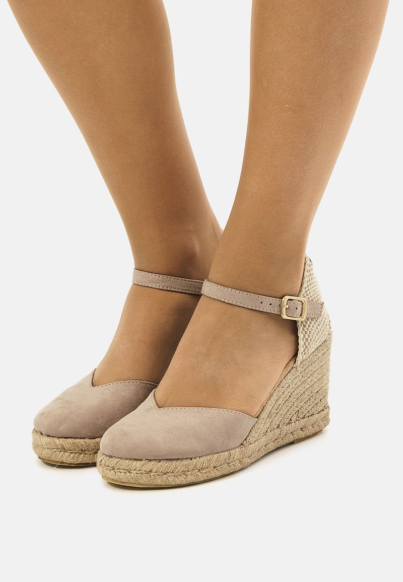 Sandales compensées en suède beige avec bride de cheville, détail en jute tressé et bout fermé. Tige texturée et finition lisse.